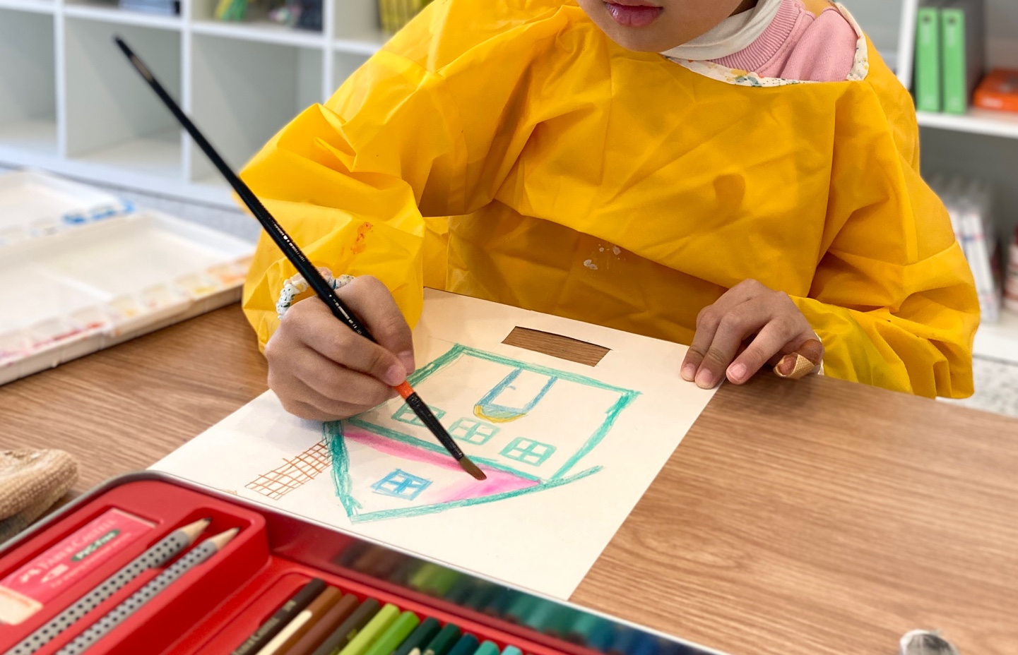 노란 가운을 입은 아이가 분홍색 집을 그리는 모습